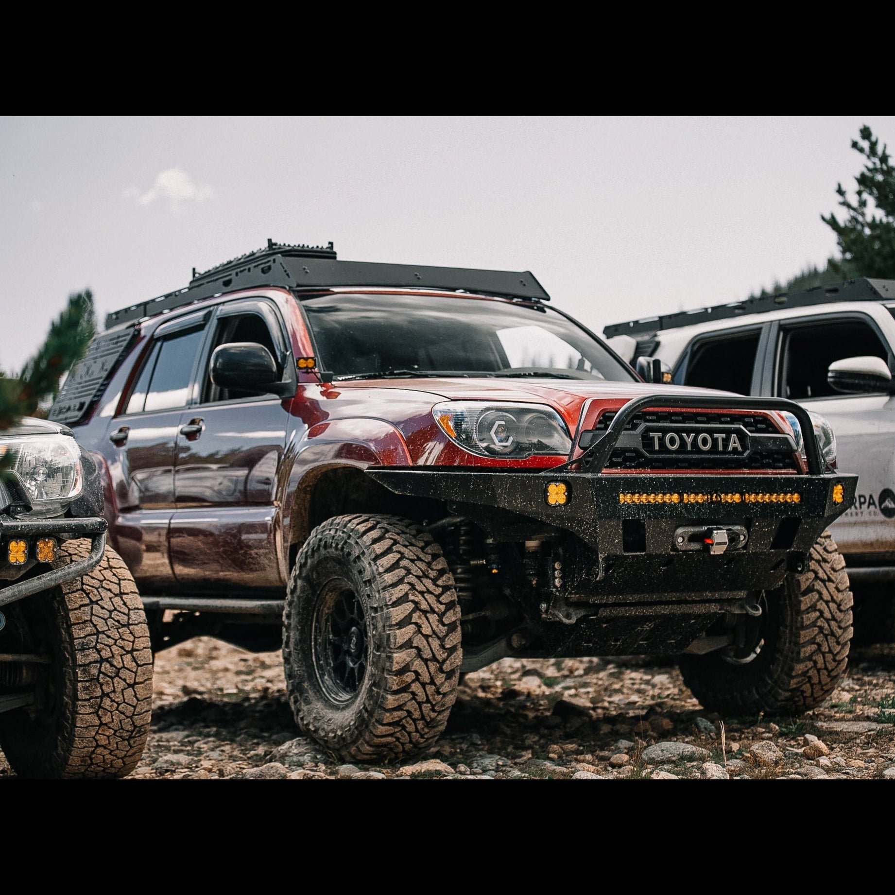 Close-up of a maroon 4Runner with a C4 winch bumper in a line of other well-equipped Toyota trucks.