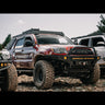Close-up of a maroon 4Runner with a C4 winch bumper in a line of other well-equipped Toyota trucks.