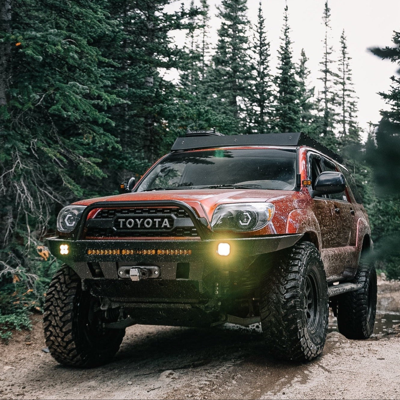 Maroon 4Runner equipped with a C4 Overland front winch bumper navigating a muddy trail in the mountains.