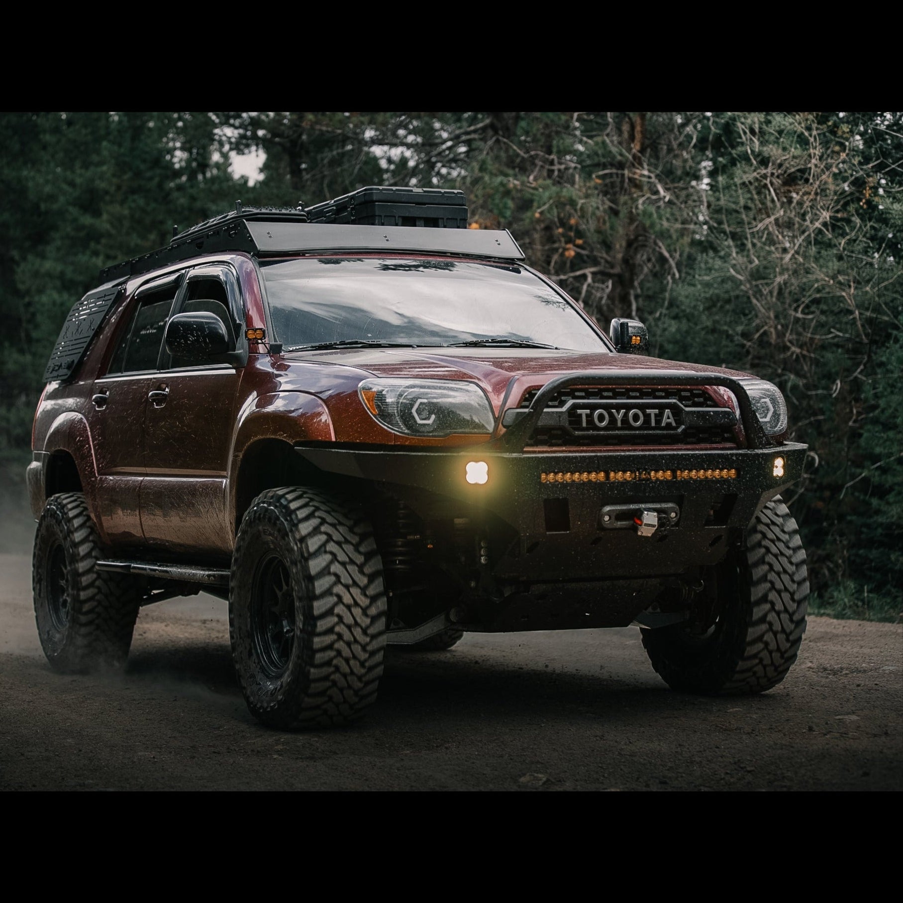 Action shot of a maroon 4Runner with C4 Overland bumper and Sherpa roof rack driving down a dirt road at speed, kicking up dust.