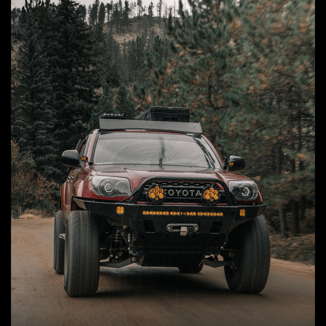 Rolling photo of a 4th Gen 4Runner driving at speed down a mountain road, equipped with a Sherpa roof rack, 35" tires and a C4 Fabrications Overland winch bumper.