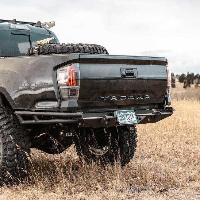 Rear quartering show showing a black wide-body Tacoma with the C4 High Clearance Rock Runner Rear bumper. 