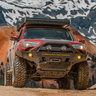 Low angle slightly quartering view of a maroon 4Runner offroading in the mountains and equipped with a C4 Overland bumper. 