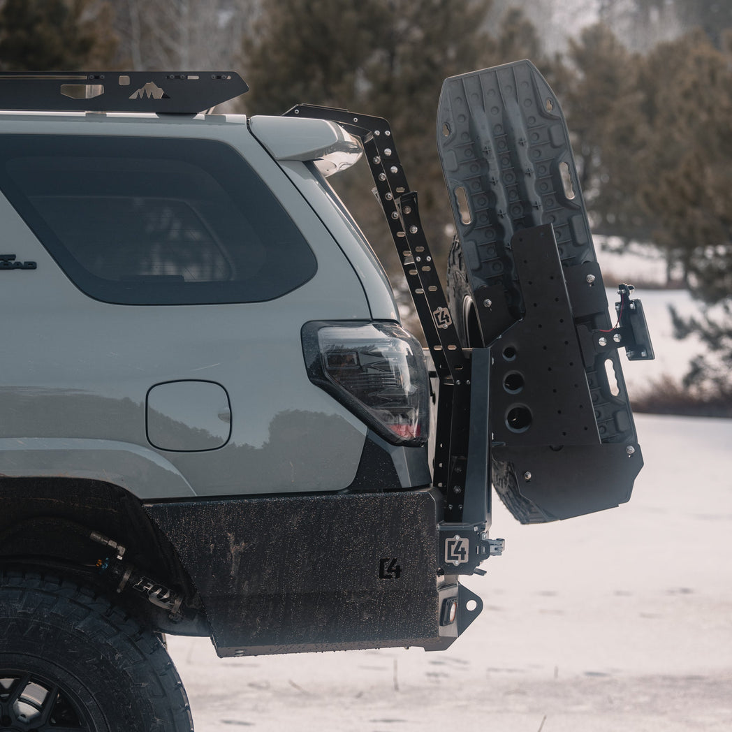 Side view of the C4 Fabrications rear bumper for the 5th Gen 4Runner, along with a hatch ladder, MaxTrax and its spare tire all on a grey 4Runner in snow-bound terrain.