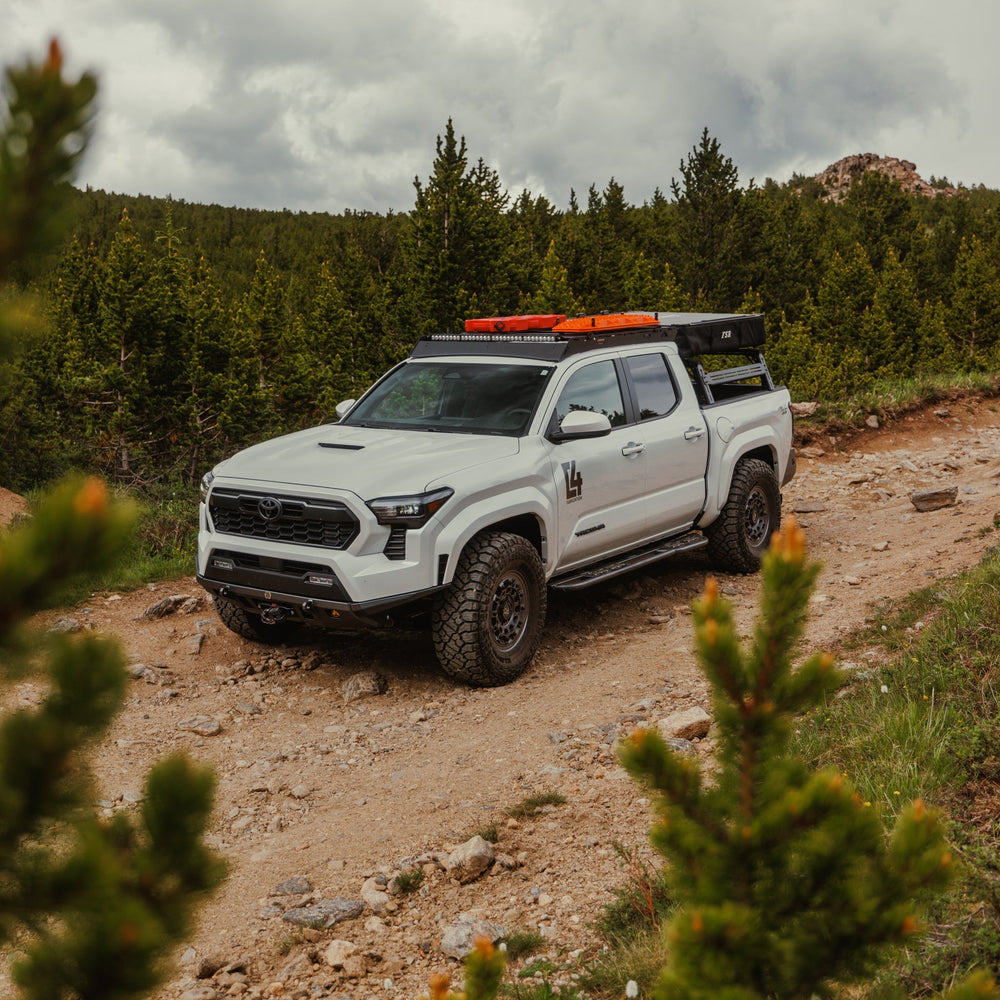 White Tacoma on a mountain pass road with a number of overlanding accessories equipped, including the sleek Lo-Pro winch bumper from C4 Fabrications.