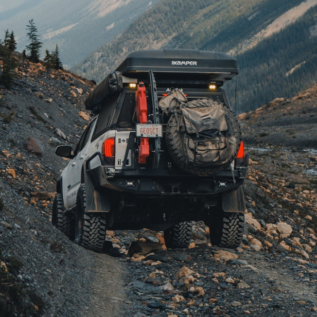 Overland-equipped white Tacoma with a roof top tent and the C4 High Clearance Rear Bumper off-road in the mountians.