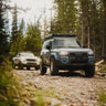 C4 Fabrications armor-equipped Land Cruiser LC250 and 2024 Tacoma driving up a rocky trail.