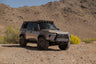 Off-road GX 550 fully equipped with off road bumpers, roof rack, light brackets, and molle panels in a desert landscape with mountains in the background