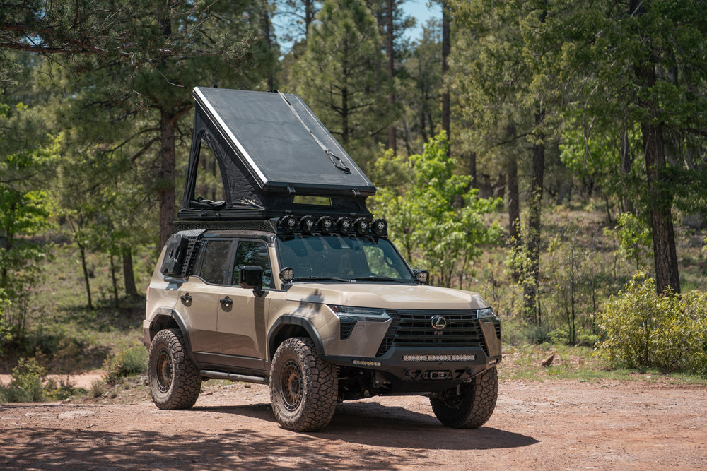Roof top tent pitched up on a GX 550 fully equipped on camping trip. Visible are off road bumpers, a roof rack, tent, light brackets, and molle panels.