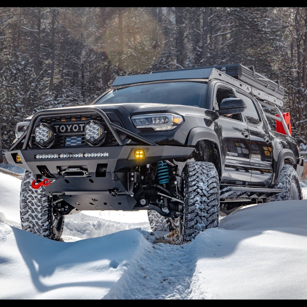 Black four-door Tacoma wheeling in the snow with an Overland winch bumper.