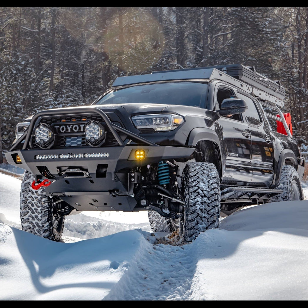 Black four-door Tacoma wheeling in the snow with an Overland winch bumper.
