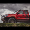 Low-angle side view from a distance of a red extended cab 2nd Generation Tacoma with the C4 Overland winch bumper installed.