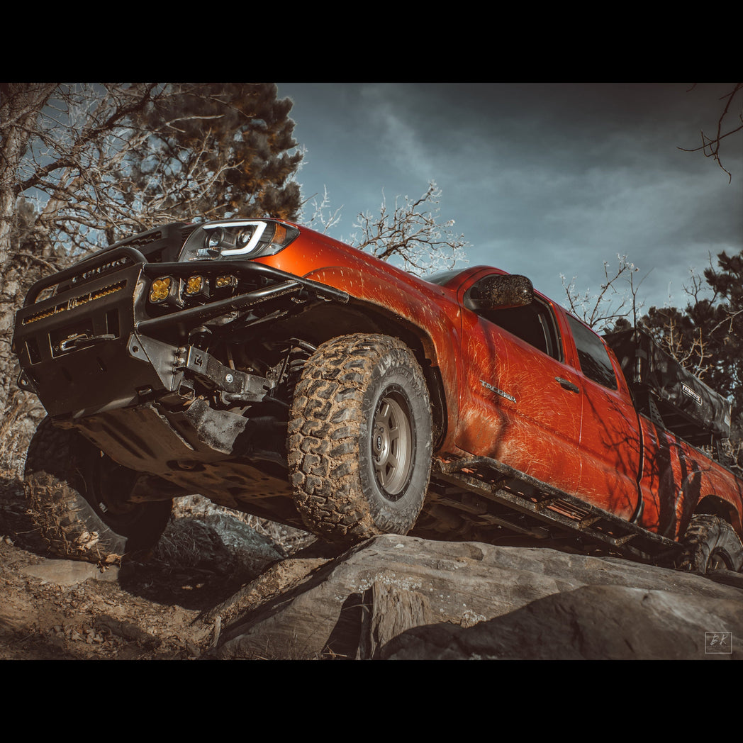 Low angle shot of a red Tacoma climbing rocks with a C4 Fabrication winch bumper.